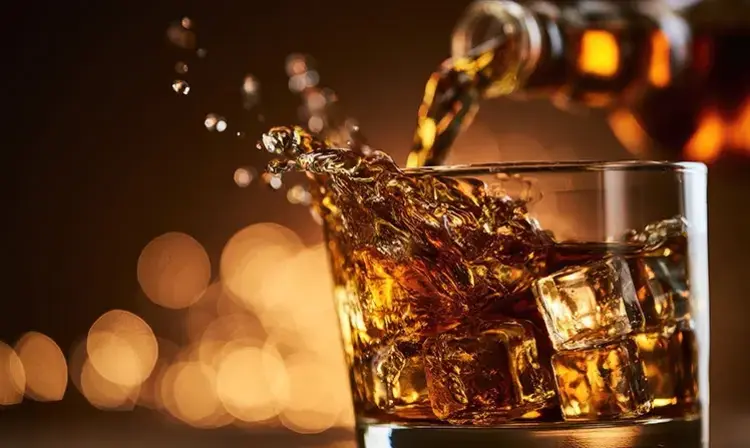 a glass of liquid with ice and a bottle