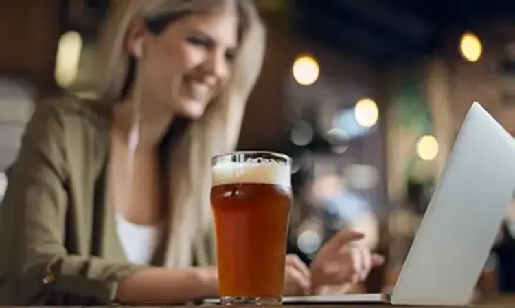 a woman looking at a computer with a glass of beer